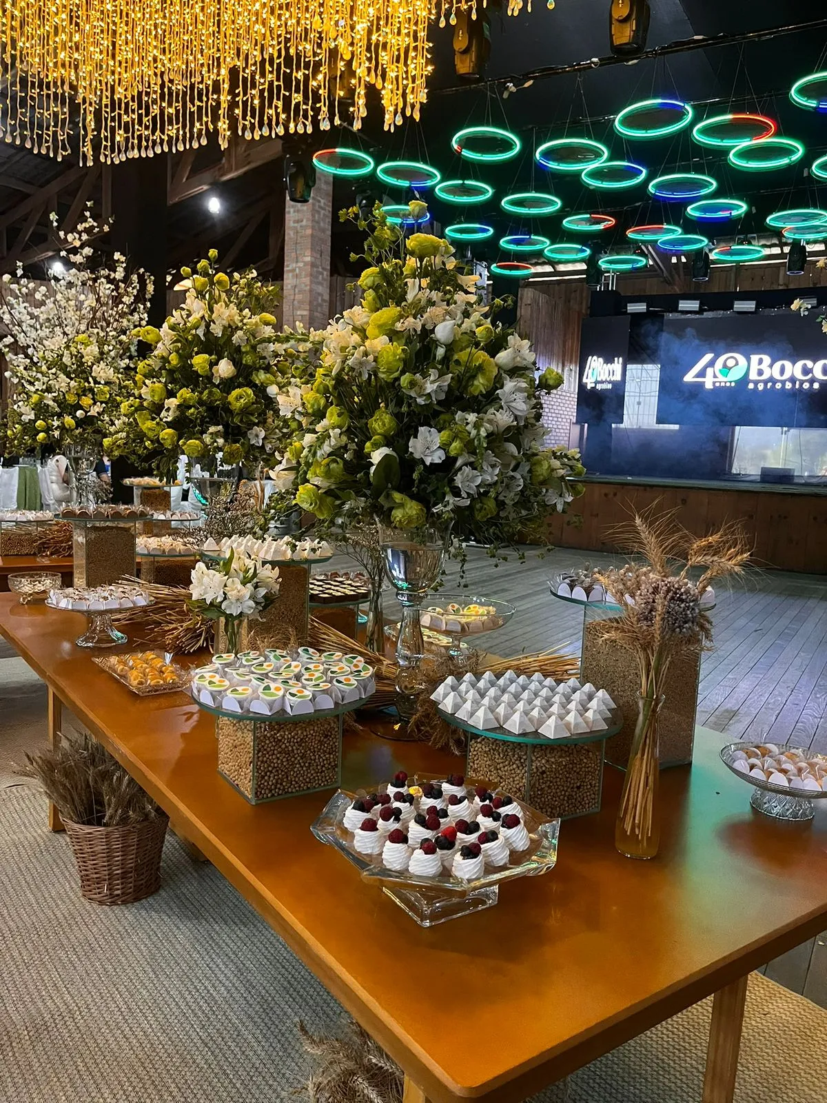 Decoração de evento corporativo com arranjos florais e mesa de doces